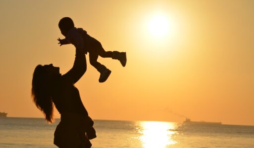 silhouette photo of a mother carrying her baby at beach during golden hour