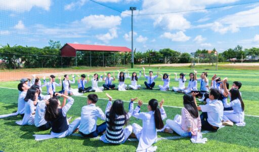 people sitting on green lawn grass while doing hands up at daytime